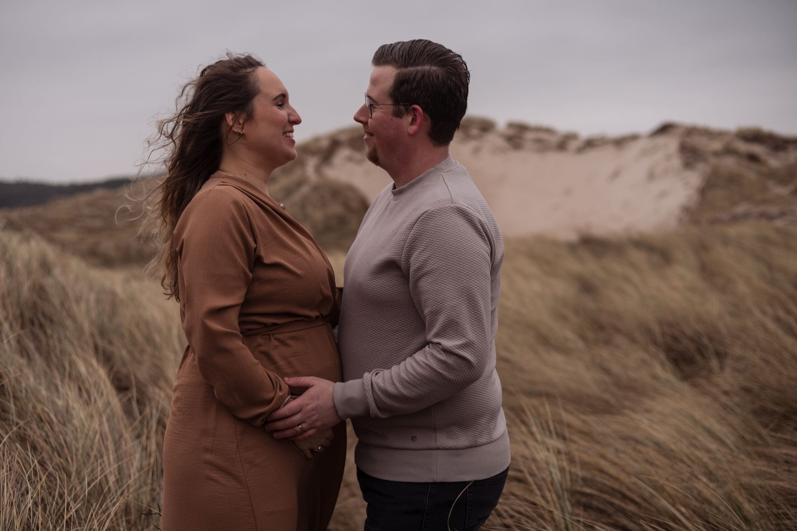 zwangere vrouw in lange roestbruine jurk met partner tijdens zwangerschapsshoot
